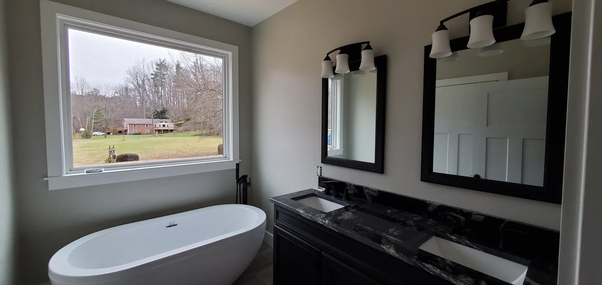 Primary bathroom with a freestanding tub, dark double vanity and black-framed mirrors in a Candler, NC custom home
