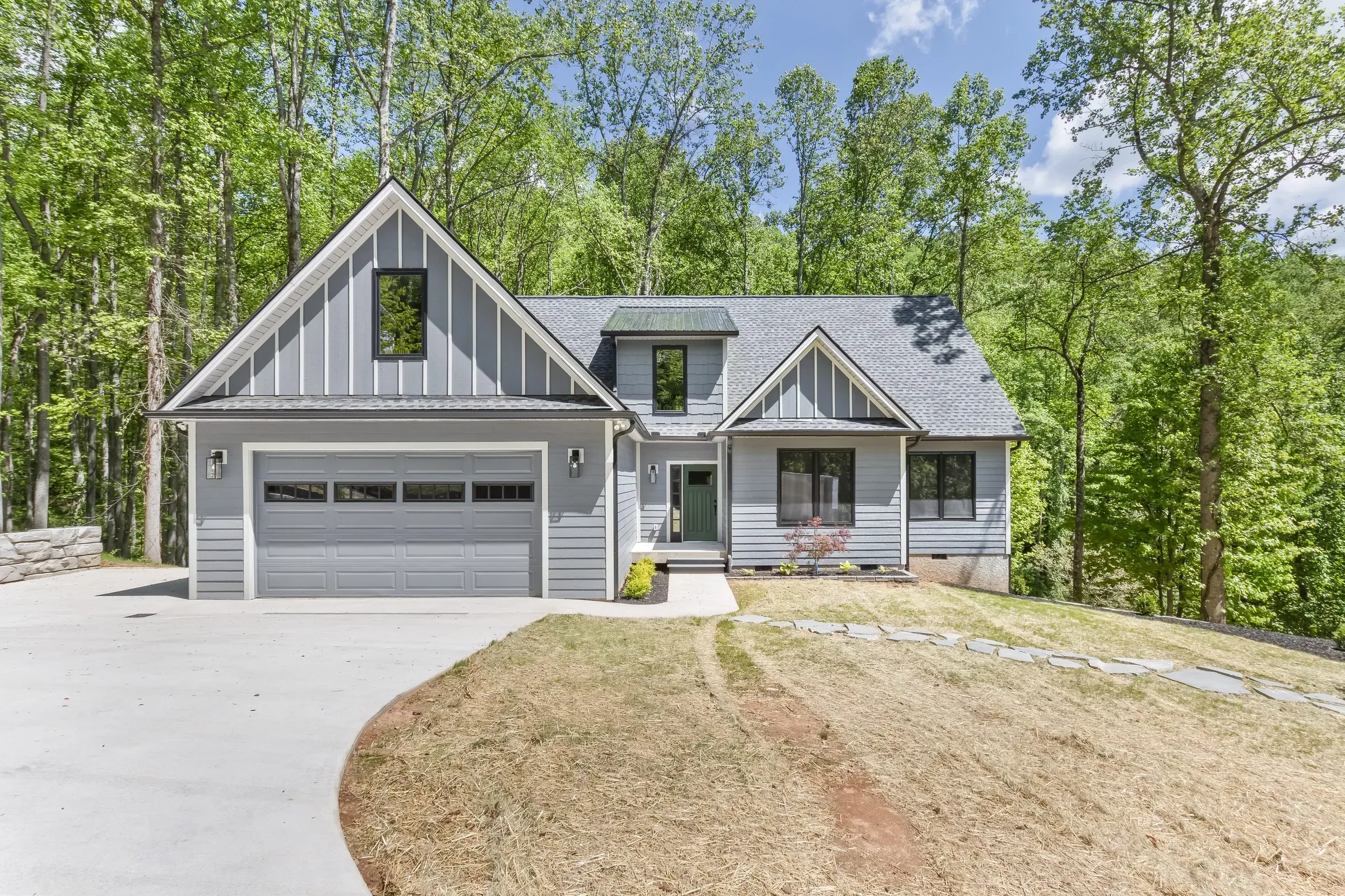 New custom home with gray lap siding, board-and-batten gables and a two-car garage on a wooded lot in Candler, NC, built by Buckingham Builders