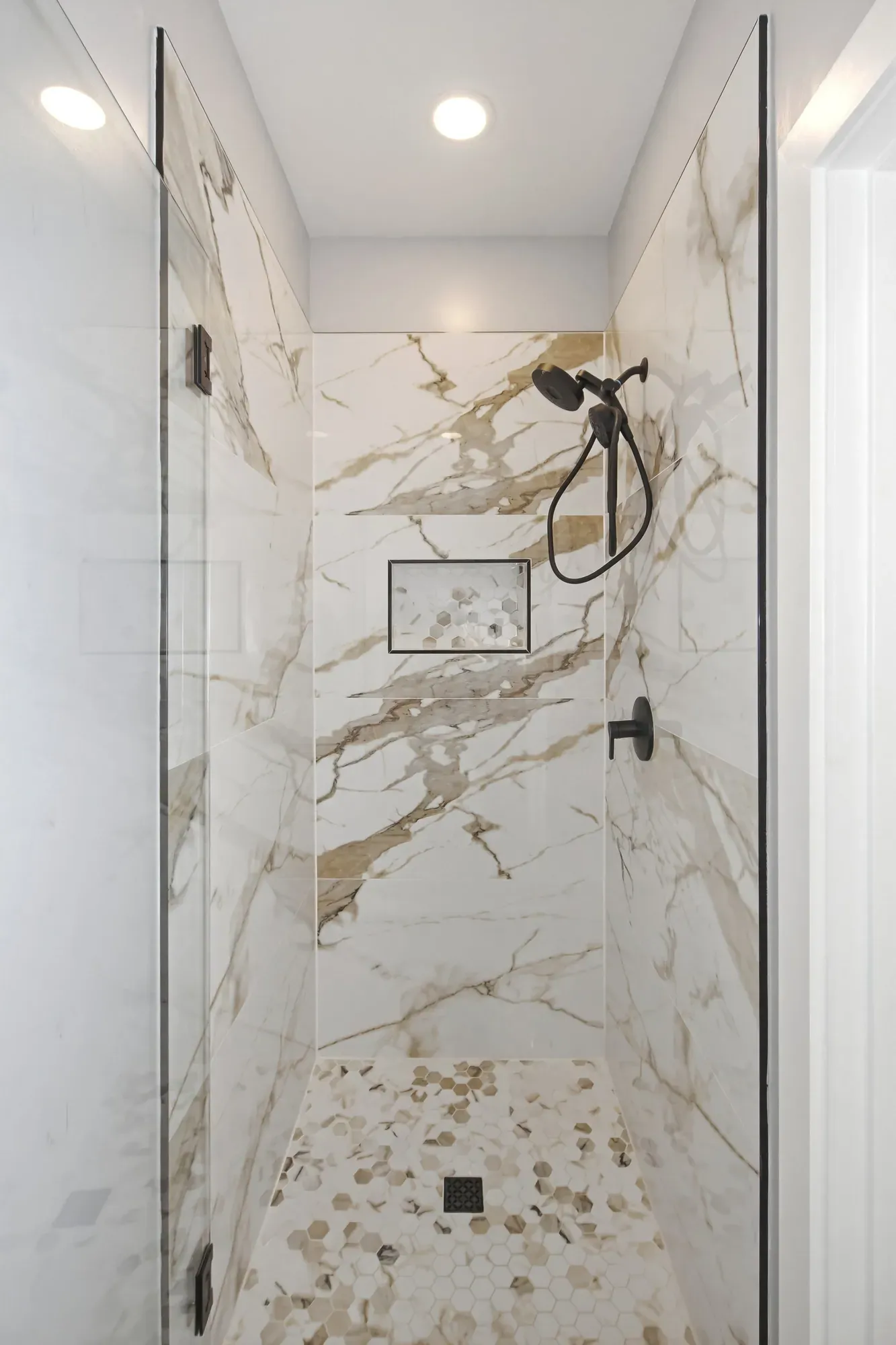 Walk-in shower with marble-look tile, a mosaic niche and black fixtures in a new Candler, NC custom home