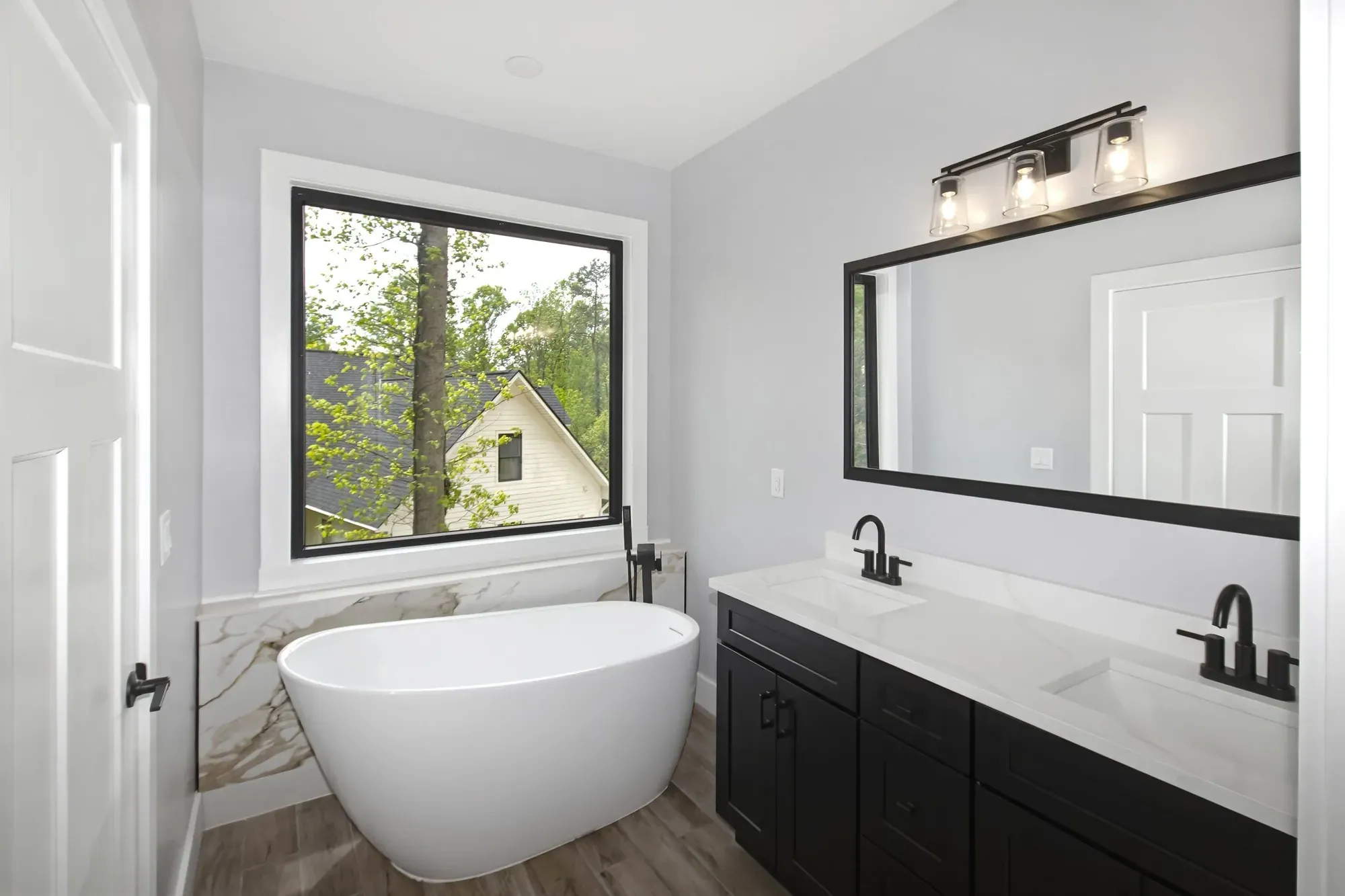 Primary bath with a freestanding tub, black vanity and wide mirror in a new Candler, NC custom home