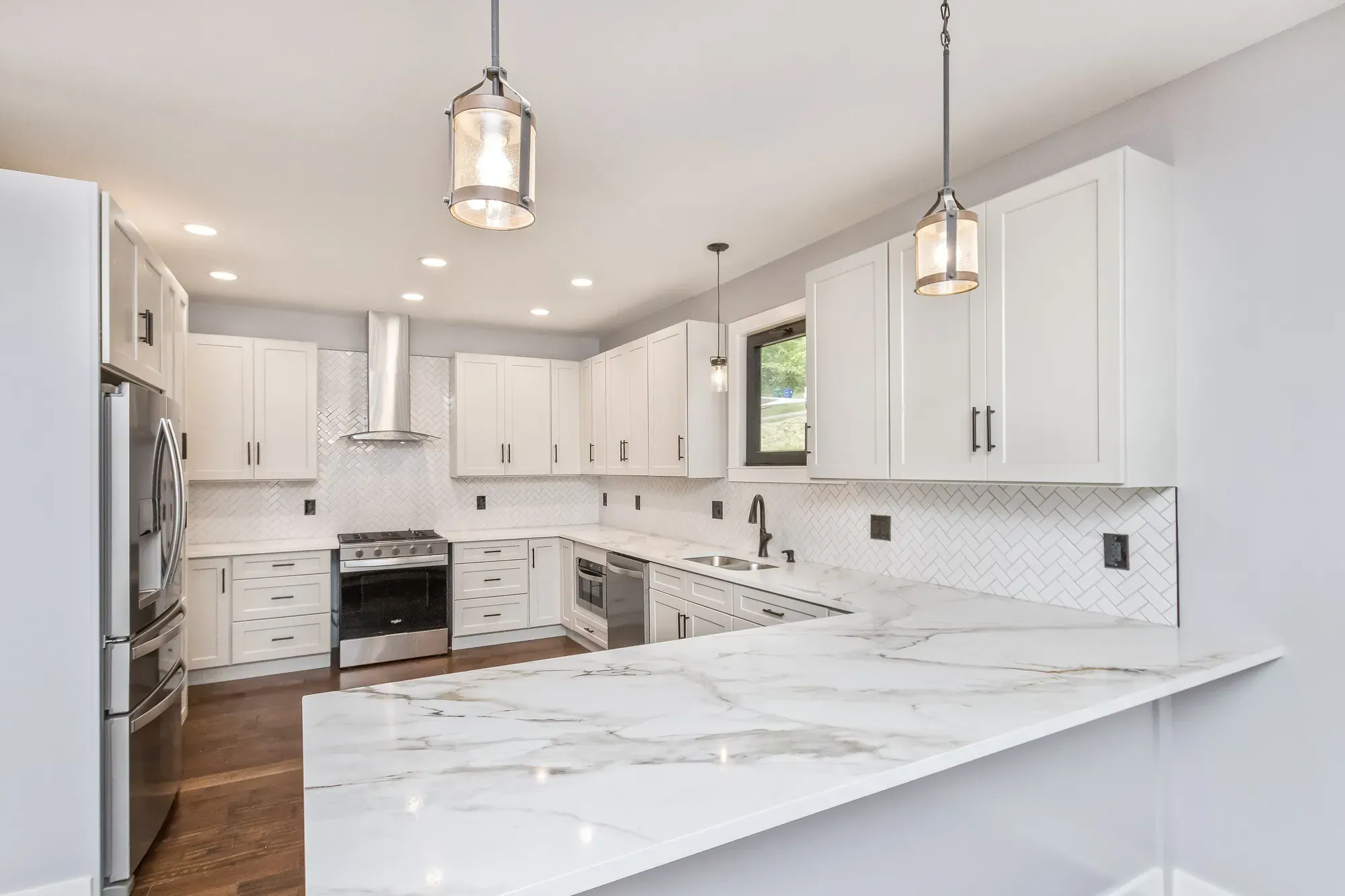 White shaker kitchen with marble-look counters and a herringbone tile backsplash in a new Candler, NC custom home